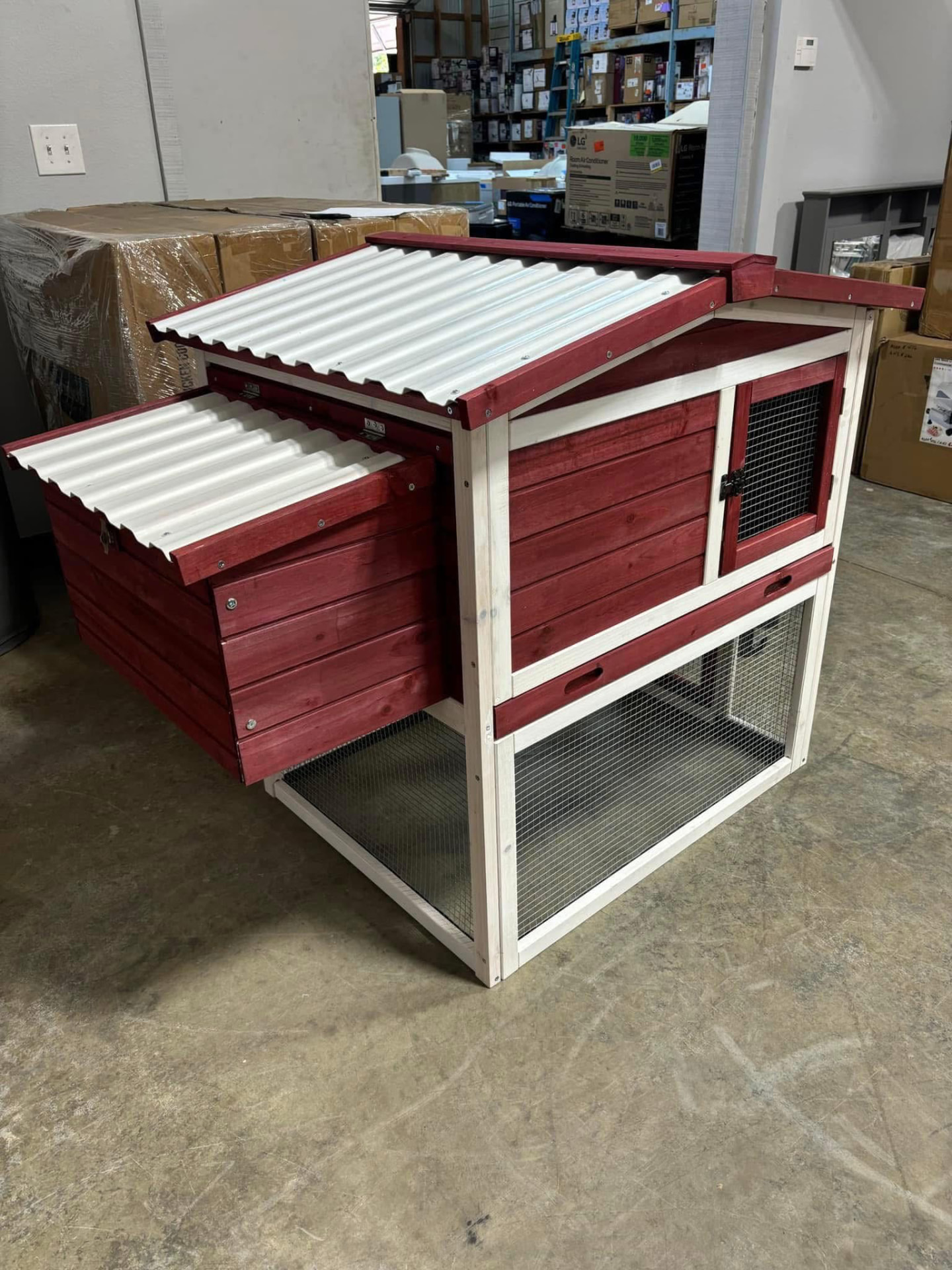 Assembled red and white wooden chicken coop with corrugated roof panels inside the store