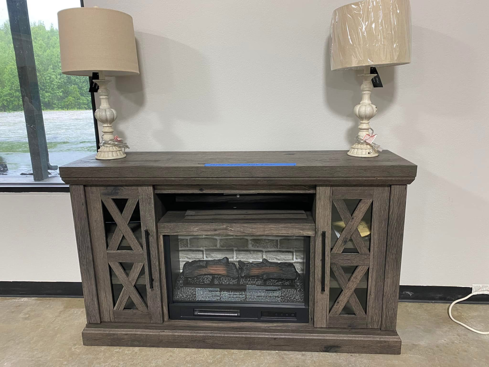 Grey wood electric fireplace media console with two cream table lamps on top