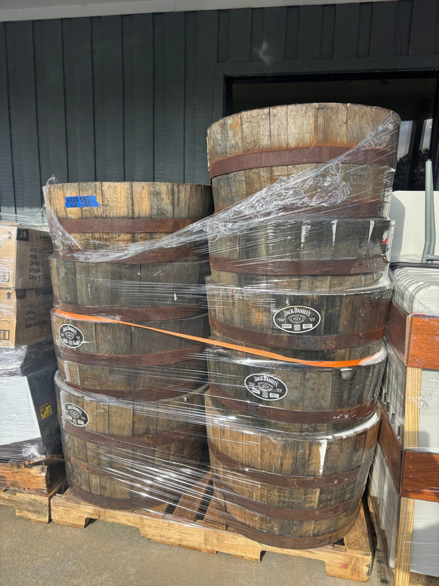 Pallet of authentic oak whiskey barrel halves used as outdoor planters, wrapped and stacked outside the store